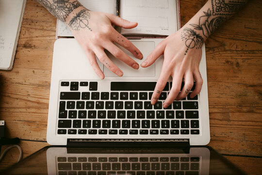 Crop tattooed woman using laptop