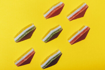 Set of colorful triangular jelly candy lined up on yellow background. Multi-colored marmalade jelly candy's. Top view.