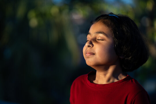 Little girl with closed eyes taking deep breath in sunset light practising yoga