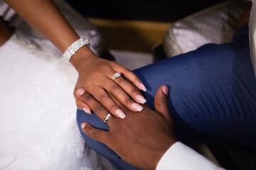 Obraz na płótnie Canvas Just married young African couple's hands, holding together, new golden rings with diamonds, long fingers, wedding manicure, shiny wedding bracelet, white dress, blue groom's suit, white shirt