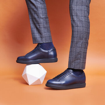 A man in blue sneakers put his foot on a white plaster figure.