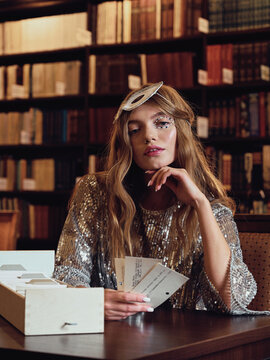 Young beautiful fashionable model sits in a library and plays cards
