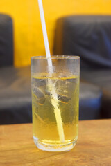 Honey lemon green tea with ice in glass with black drinking straw on table with blurred background