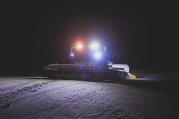 Snowcat bulldozer with multicolored light drives on the slopes and maintenance on the mountains ski resort