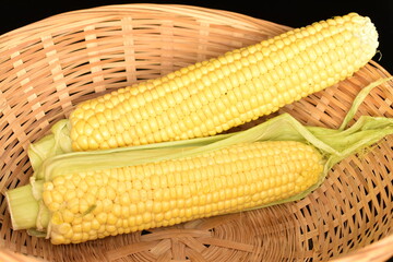 Ripe corn cobs, close-up, in straw dishes.