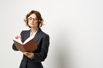 Woman at work with book in hand light background classic suit glasses head