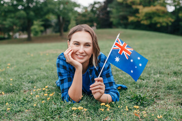Happy Caucasian middle age woman waving Australian flag. Smiling proud citizen lying on green on...