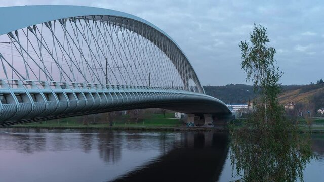 
time lapse of the flowing Vltava river and the modern white transport bridge and the movement of traffic on it in Prague in November 2020 and in the sky with clouds moving