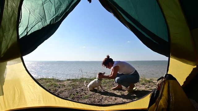View from a tourist tent on a woman playing with a dog on the seashore. The girl set up camp in the countryside.