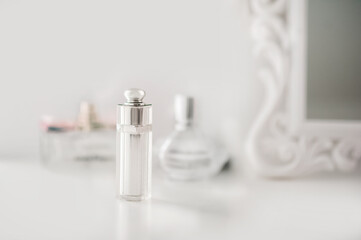 The bottle is on the dresser in the white bedroom. Perfume in a bright interior. White boudoir table close up and copy space.