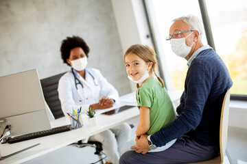 Obraz premium Grandfather with protective facial masks with granddaughter at black female doctor