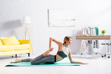 Fototapeta na wymiar Barefoot sportswoman practicing yoga while lying on fitness mat
