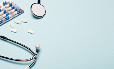 Pills and stethoscope on a light blue background. Copy space. Medical concept