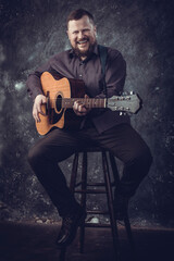 Mature musician plays acoustic guitar emotional studio portrait.