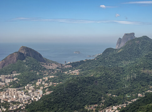 Rio De Janeiro, Brazil - December 24, 2008: Aerial View Of Green Forested Hills Down From Christ The Redeemer With Lower Lying Neghborhoods With Buldings. Blue Ocean Under Hazy Light Blue Sky.