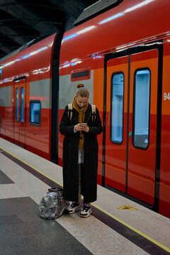 a woman takes a travel photo for a blog on her smartphone in front of a red high speed train in moscow russia