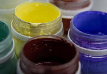 Jars of acrylic paint in red, yellow, purple shades close-up.