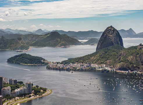 Rio de Janeiro, Brazil - December 24, 2008: Aerial view on Sugarloaf mountain and the entrance to bay with Praia da Urca neighborhood and its yacht harbor under azure cloudscape. Muntains on horizon.