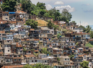 Fototapeta na wymiar Rio de Janeiro, Brazil - December 24, 2008: Part of favela on mountain slope under blue cloudscape. Mass of poor houses on top of each other and some green foliage.