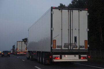 Semi trailer trucks van move on dry asphalted evening road in dusk, back view - intrenational transportation logistics