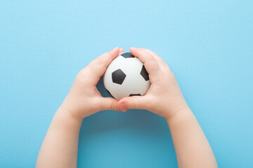 Baby boy hands holding and playing with white black football ball on light blue floor background. Pastel color. Closeup. Toys of development for infant. Point of view shot. Top down view. - Powered by Adobe