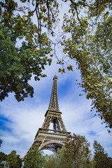 Looking up at the Eiffel Tower in Paris through the trees with a blue cloudy sky
