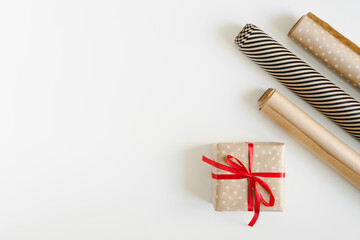 Christmas gift wrapping idea. Gift box with red ribbon and kraft paper rolls. DIY eco friendly present wrapping