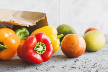 Fruits and vegetables on concrete background. Healthy diet. Bell peppers, orange, avocado and mango delivered in paper bag
