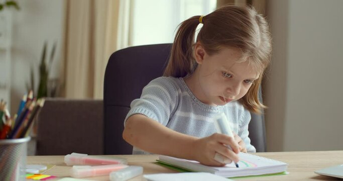 Portrait of cute concentrated little caucasian kid girl draw color pencil marker sitting at home table. Pretty preschool child coloring picture enjoy creative activity relax children distant education
