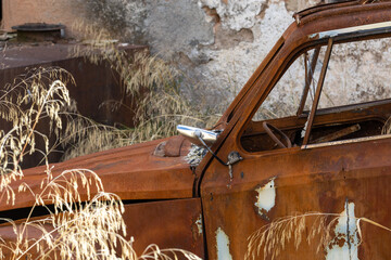 Burned and rusty car abandoned in the field next to a ruined house