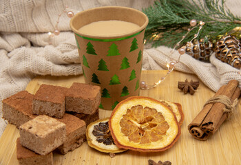 Cardboard disposable Christmas glass with a drink and various sweets and aromatic spices on a wooden tray .
