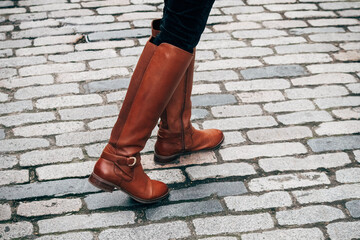 woman in boots crosses cobblestone road