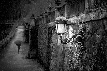 Primer plano de un farol en el muro de un parque y con la silueta de una persona con un paraguas 