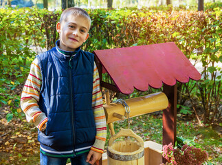 Baby boy stands near the well in autumn on a Sunny day. Beautiful autumn photos with children.
