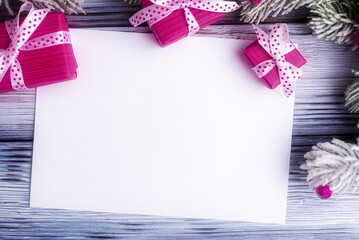 White blank paper sheet with pink gift boxes and Christmas decoration on light wooden background
