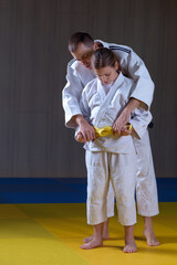 Adult black belt judoka helping beginner judo girl to tie a belt