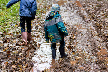 Two children wearing wellies walking through deep mud.