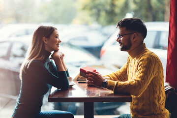 Young man surprising his beautiful girlfriend with a gift box