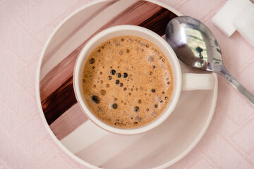 Taza de café, terrones de azúcar y cuchara  sobre un mantel rosa, visto desde arriba