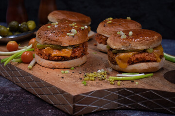 Vegan burgers made with seitan and vegan cheese, pickles on wooden cutting board