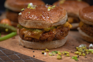 Vegan burgers made with seitan and vegan cheese, pickles on wooden cutting board