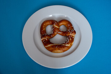 Bavarian pretzel with salt on a plain white round plate on a blue background