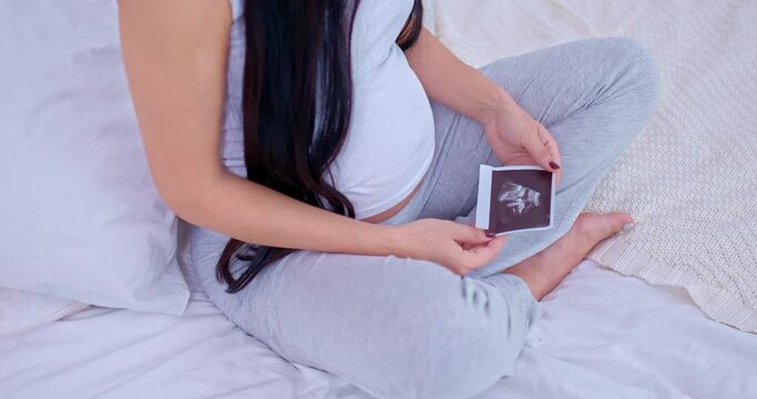 Close-up, a pregnant woman holding an ultrasound photograph of her baby in her hands, expecting a baby. Family values, caring and happy motherhood. Side view. 4k, ProRes