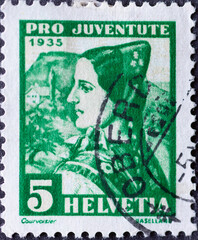 Switzerland - Circa 1935 : a postage stamp printed in the swiss showing the portrait of a woman from basel in historical costume with the village in the background