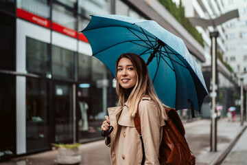 A beautiful smiling young woman walking through the city with an umbrella.