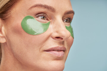 Anti aging procedures. Close up portrait of a beautiful adult lady using eye patches while standing...