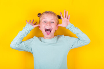 Emotional girl. Funny child girl shows tongue on yellow background. Emotions on kid face. Happy...