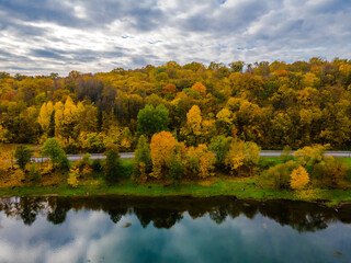 Fototapeta premium Aerial autumn view of a hill with golden trees and reflections in river