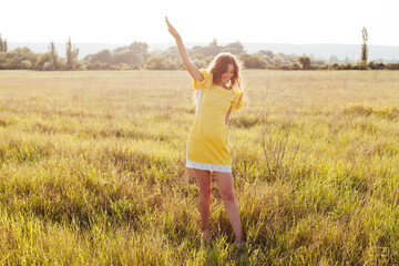 Naklejka na ściany i meble Beautiful woman in yellow dress walks on the field with flowers