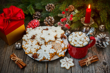 Red mug of coffee with marshmallows and gingerbread on a wooden table against a background of fir branches. Christmas still life.